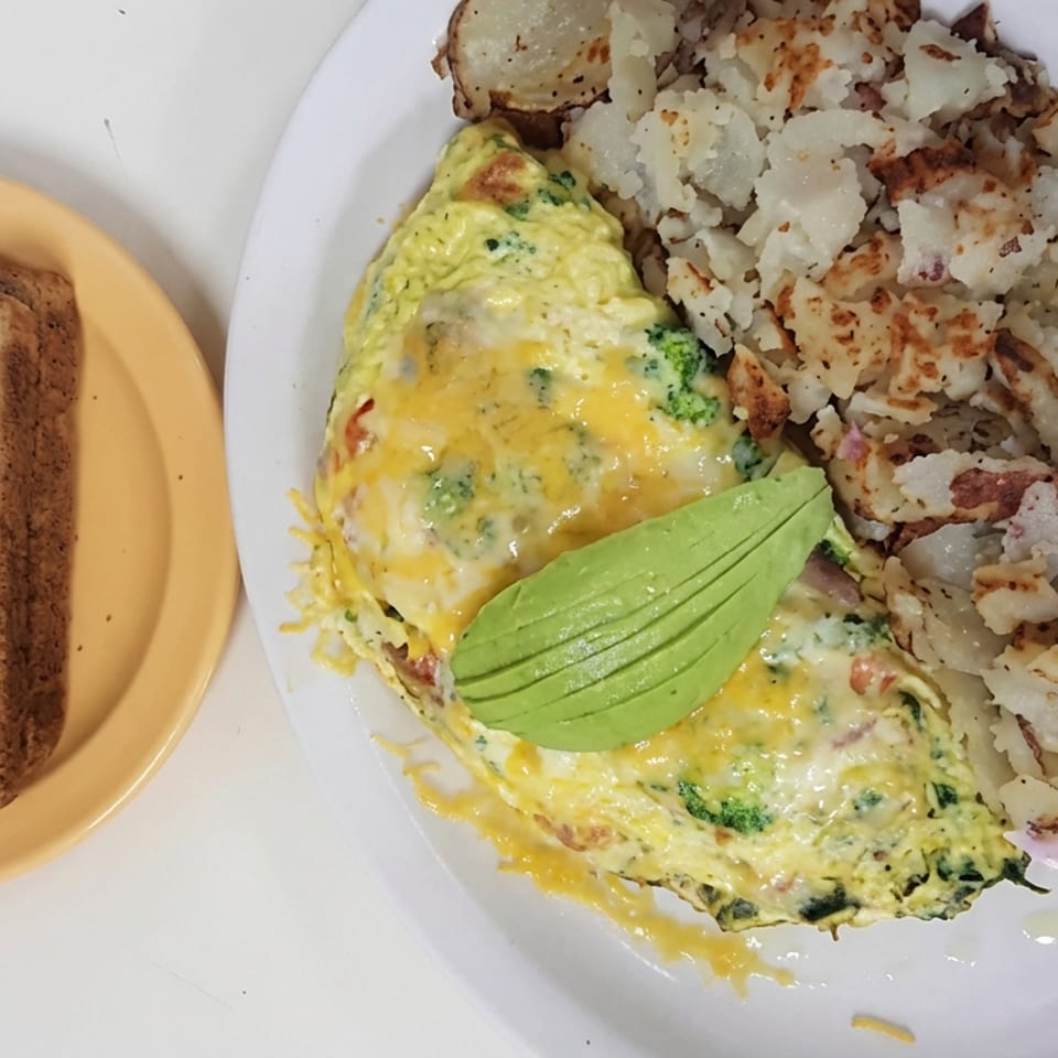 Cheesy broccoli omelet topped with avocado, served with crispy home fries and two slices of whole-grain toast.